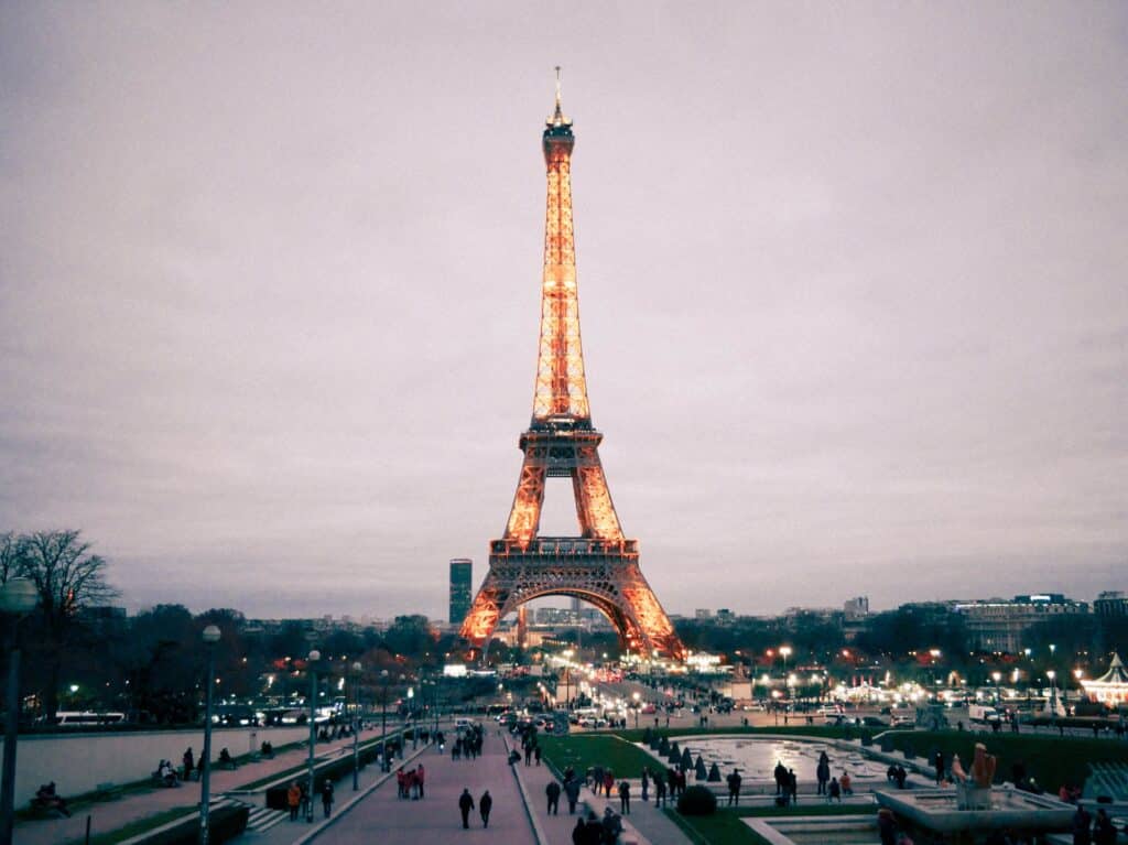 Torre Eiffel em Paris toda iluminada em um fim de tarde com muitas pessoas caminhando ao redor, para representar o melhor seguro viagem