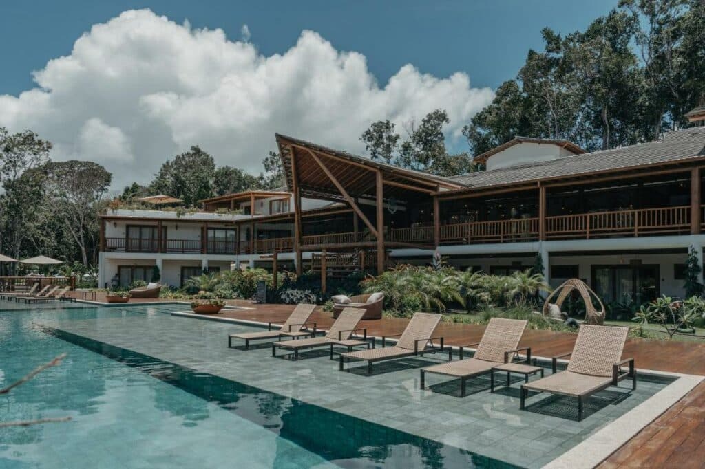 Piscina do Aysú Trancoso Hotel durante o dia com cadeiras do lado direita da imagem em frente a piscina e ao fundo a hospedagem. Representa airbnb em Trancoso.