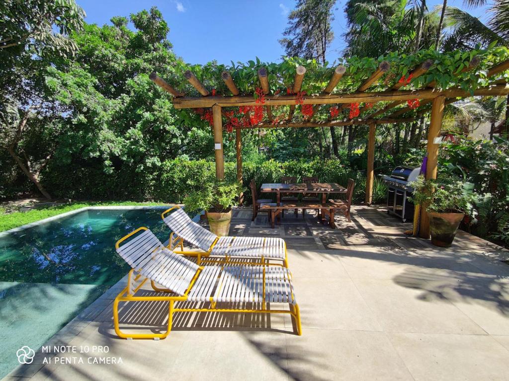 Área de piscina da Linda Casa Praia de Pauba em condominio com piscina do lado esquerdo da imagem, com cadeiras do lado direito da piscina.