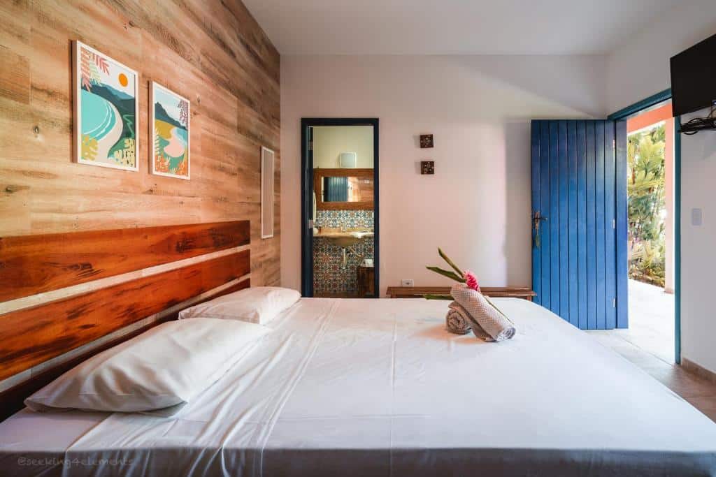 Cama de casal em quarto com parede de revestimento que lembra madeira e TV em frente à cama na Pousada Canto do Dado