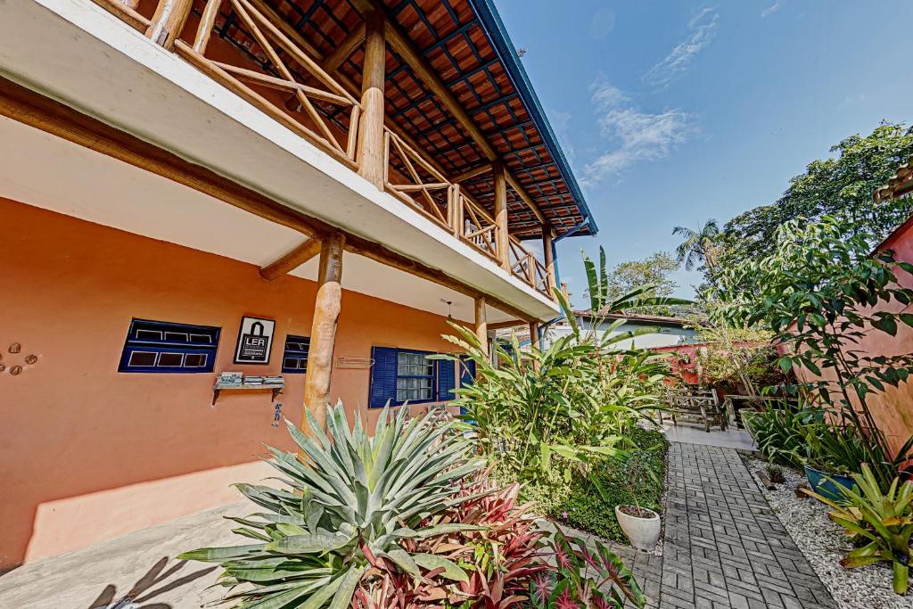 Área externa da Pousada Canto do Dado, uma das pousadas em Ubatuba. Há um prédio colorido com varanda de madeira, cercado por plantas verdes e um caminho de pedras, sob céu azul claro
