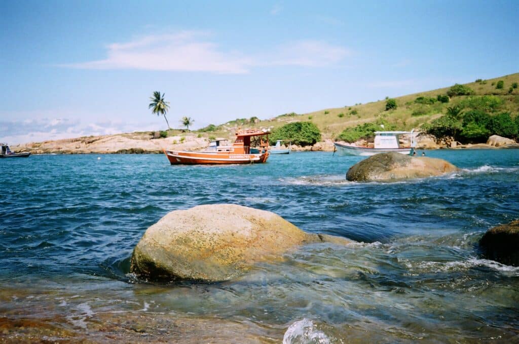 Vista da praia de Calheta em São Sebastião durante o dia com pedra a frente dentro do mar e ao fundo um barco navegando.