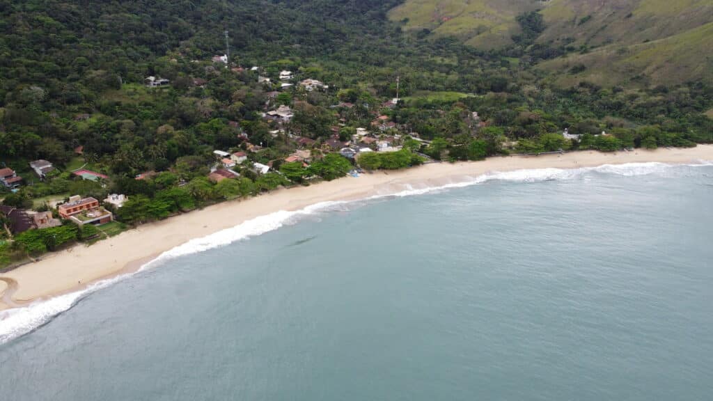 Vista da praia do Toque-Toque Grande em São Sebastião durante o dia com mar a frente, uma faixa de areia ao fundo com floresta e casas. Representa airbnb em Toque-Toque Grande.