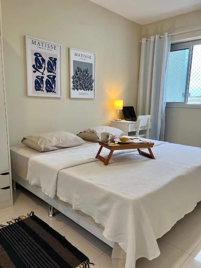 Quarto do Apartamento Bora Bora com cama de casal do lado esquerdo da imagem com uma bandeja com café da manhã em cima da cama e do lado esquerdo da imagem com uma mesa com cadeira.
