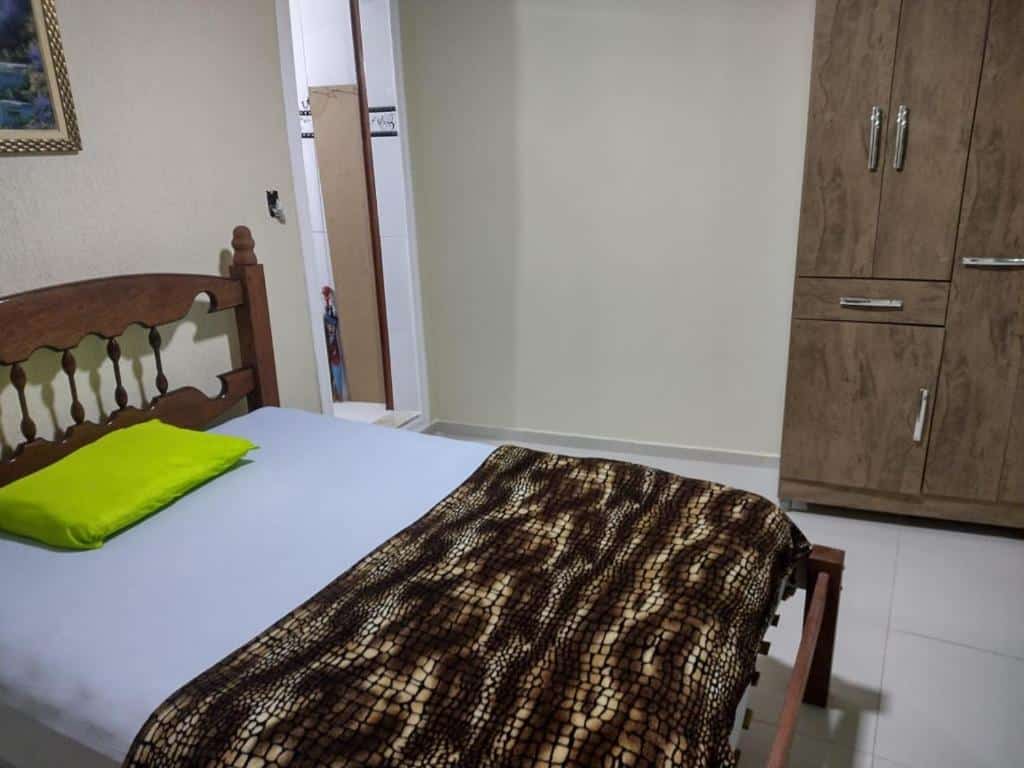 Quarto do airbnb Hospedagem da Val. A cama está encostada na parede do lado esquerdo do quarto, no lado direito da cama há uma porta que dá acesso ao banheiro e ainda no lado direito há um armário de madeira. Imagem para ilustrar o post airbnb em Angra dos Reis.