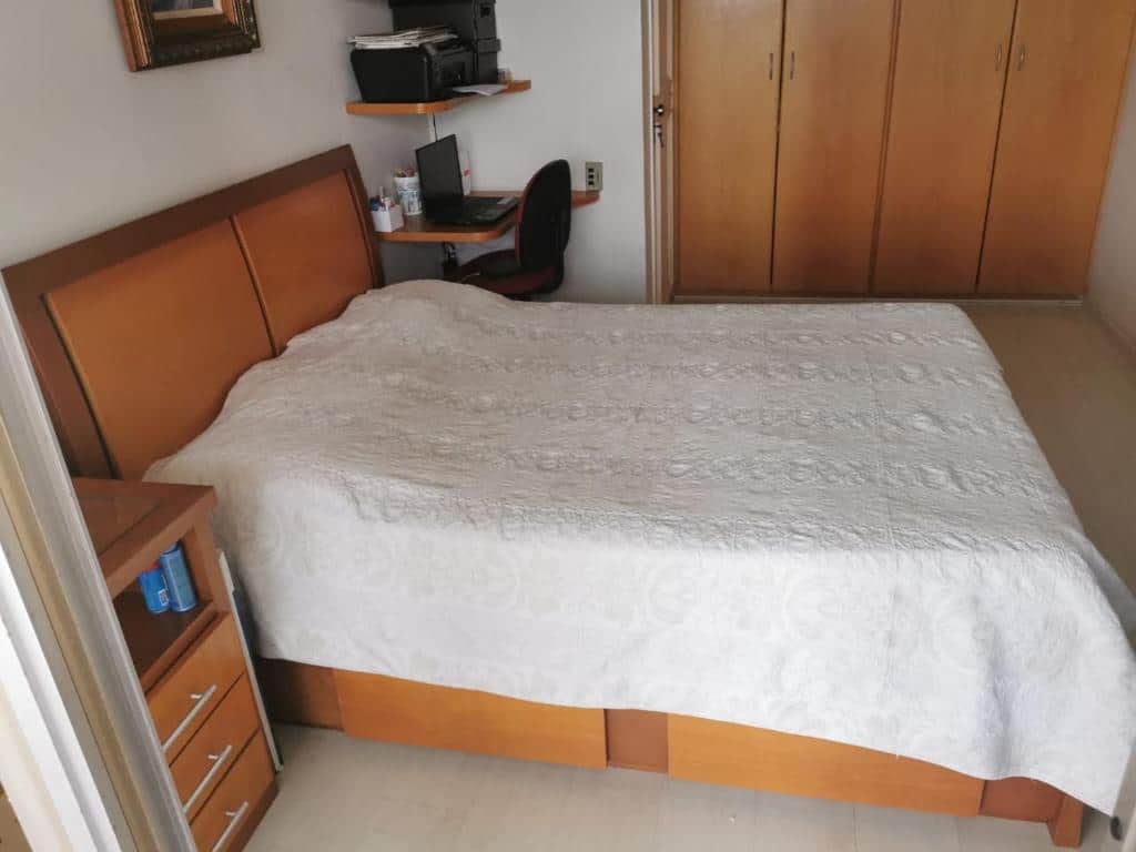 Quarto do Apartamento frente mar, Posto 5 – Barra da Tijuca com cama de casal do lado esquerdo da imagem e do lado direito da cama uma cômoda e do lado esquerdo uma cômoda com um notebook e cadeira. Representa airbnb na Barra da Tijuca.