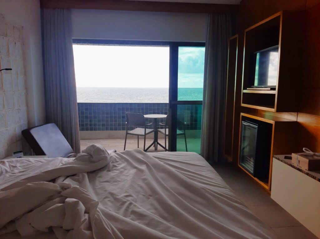 Quarto do Ritz Lagoa da Anta. Na imagem parece uma cama com o lençol mexido, e uma varanda com uma mesinha e vista do mar
