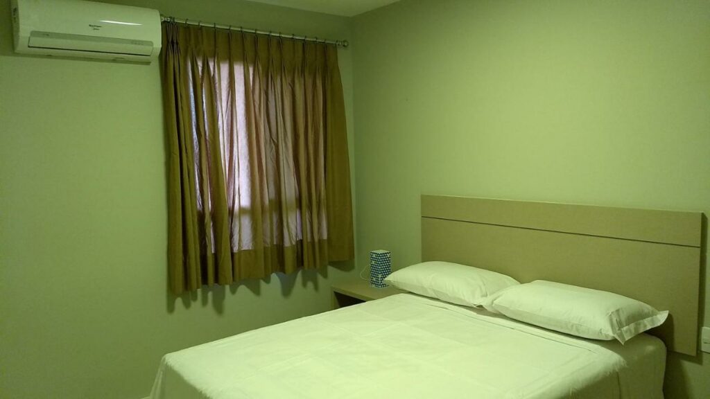 Quarto do Residencial Meireles Sollaris, um dos airbnb em Fortaleza, com cama de casal com 2 travesseiros em cima, uma mesinha ao lado esquerdo com uma luminária em cima, uma janela com a cortina fechada e um ar-condicionado