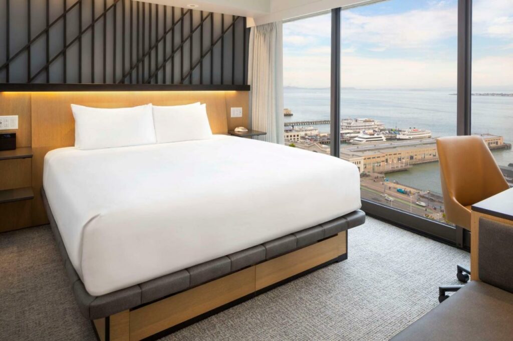 Quarto do Hyatt Regency San Francisco com cama de casal do lado esquerdo da imagem e do lado esquerdo da imagem uma mesa com cadeira. Representa hotéis em San Francisco.