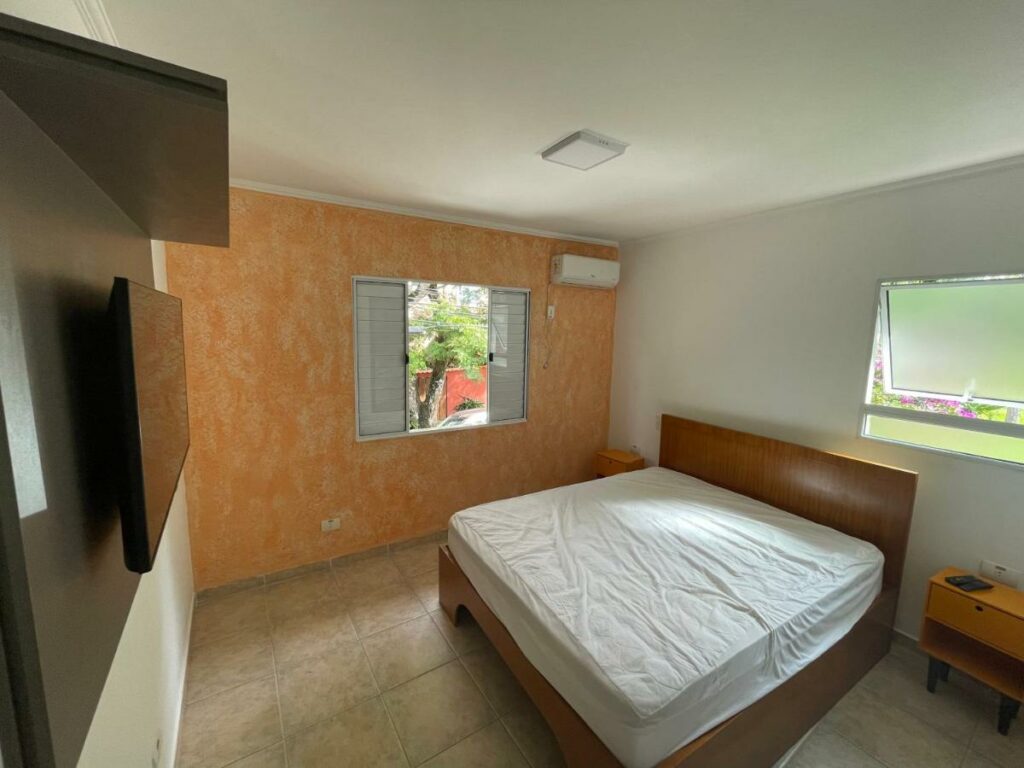 Quarto do Lar Doce Lar Toque Toque Grande  com cama de casal do lado direito da imagem com uma cômoda em cada lado com uma TV a frente presa na parede. Representa airbnb na praia de Calhetas.