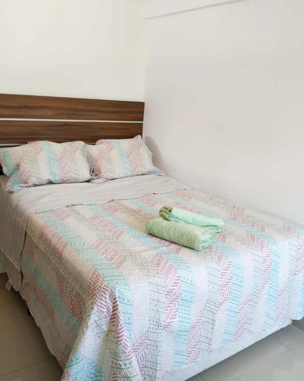 A cama de casal possui uma cabeceira de madeira e está encostada na parede do lado direito do quarto. Imagem para ilustrar o post airbnb em Angra dos Reis.
