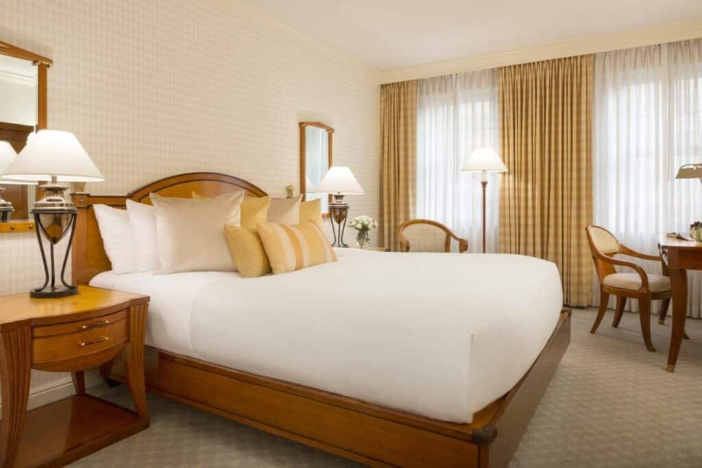 Quarto do Orchard Hotel com cama de casal do lado esquerdo da imagem com uma cômoda em cada lado da cama com luminária e do lado esquerdo da imagem uma cômoda com cadeira. Representa hotéis em San Francisco.