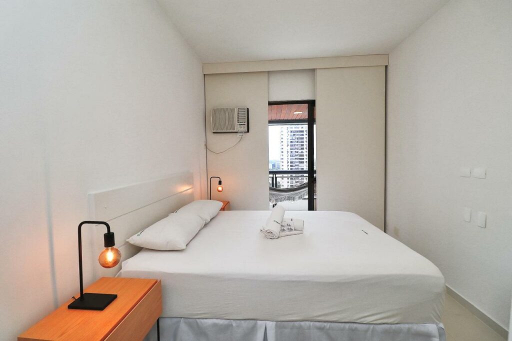 Quarto do Rio Spot Alfa Barra U044 com cama de casal do lado esquerdo da imagem em cada lado da cama uma cômoda com luminária. Representa airbnb na Barra da Tijuca.