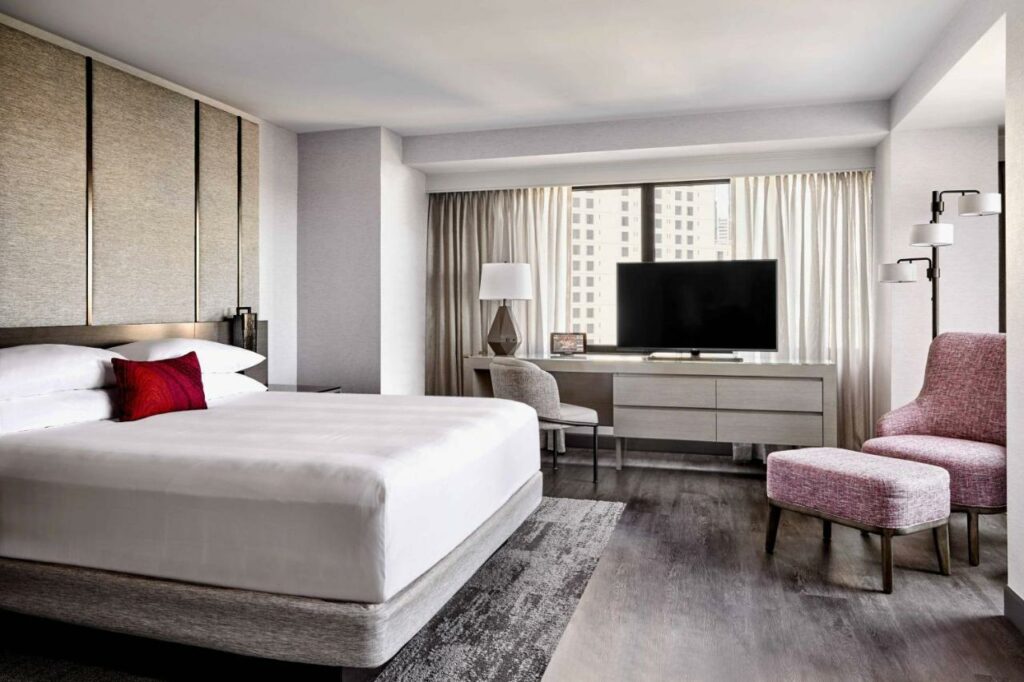 Quarto do San Francisco Marriott Marquis Union Square com cama de casal do lado esquerdo da imagem, em frente a cama uma poltrona e do lado esquerdo da imagem uma cômoda com TV.