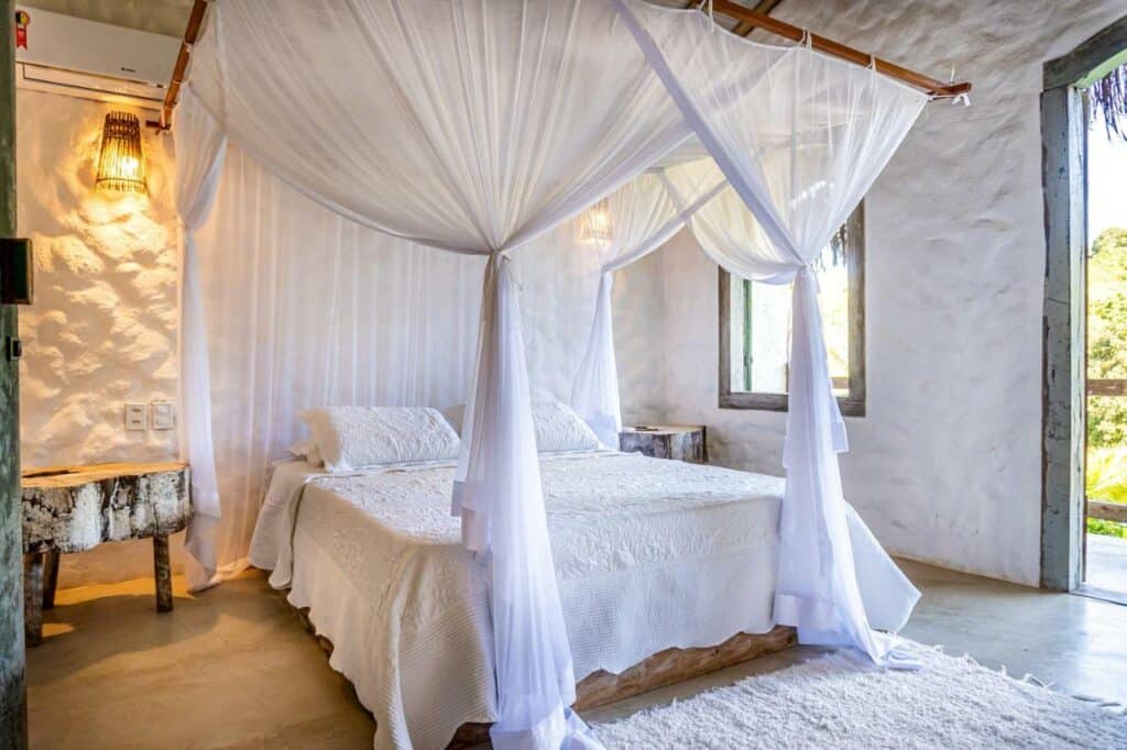 Quarto da Vila Rudá Trancoso com cama de casal no centro da imagem e em cada lado da cama uma cômoda. Representa airbnb em Trancoso.