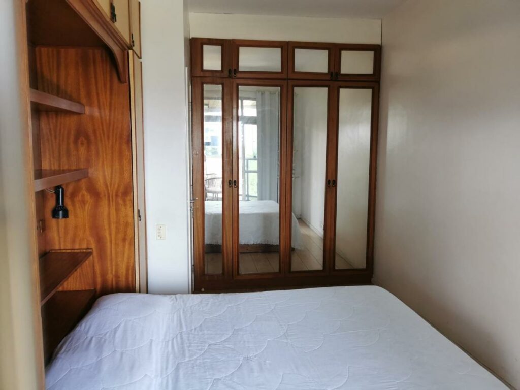 Quarto do Vistão do mar – posto 5 Barra da Tijuca com cama de casal do lado esquerdo da imagem a frente e ao fundo o guarda-roupa. Representa airbnb na Barra da Tijuca.