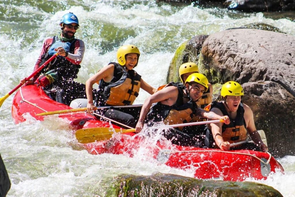 Pessoas em um bote praticando rafting com água espirrando para vários lados. Algumas pessoas estão sorrindo e outras estão com a boca aberta como se estivessem surpresas com a adrenalina. A imagem mostra como é o passeio de Rafting no rio Chili, oferecido pela Civitatis. Foto: Civitatis
