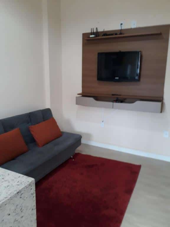 Sala de estar do Recanto Vovô João com um sofá na parte esquerda da foto, um tapete no pé do sofá e na parede do lado do sofá bem ao centro da sala tem uma tv. Imagem ilustrando post Airbnb em Cunha.