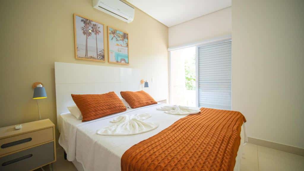 Quarto do Residencial Las Salinas. Uma cama de casal está no meio, ao lado de uma mesinha com duas gavetas e um abajur. Do outro lado, ao fundo, há uma janela.