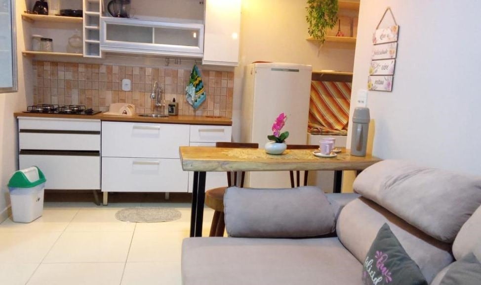 Sala de estar do Residencial Temporada Aracaju. Um sofá do lado direito, com uma pequena mesa para duas cadeiras. Atrás a cozinha.