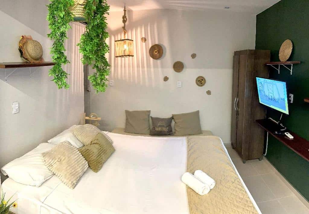 Quarto do Residencial Temporada Aracaju. Uma cama de casal do lado esquerdo, de frente uma prateleira, uma televisão e um guarda-roupa. No fundo um sofá cama com almofadas.
