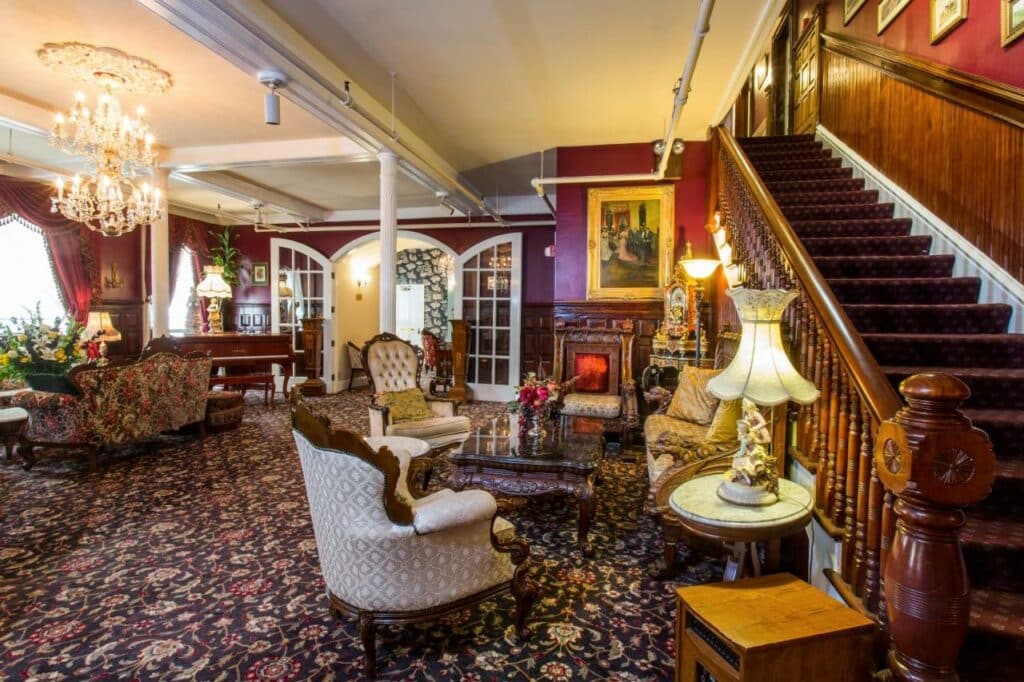 Sala de estar do Queen Anne com escada do lado direito da imagem do lado esquerdo a sala com poltronas e luminárias.