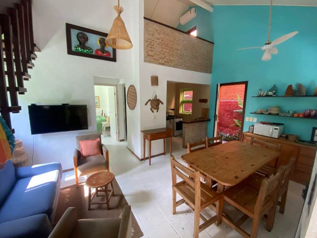 Sala de estar da Vila dos Tangarás, Casa 1 Praia, a 30m do mar com sofá e do lado esquerdo da imagem com duas poltronas e uma TV e do lado direito uma mesa de jantar com armário ao lado.