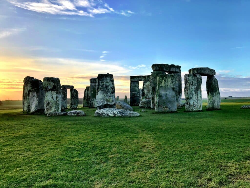 vista do Stonehenge, um monumento de pedras sobrepostas com muita grama ao redor e céu azul na Inglaterra