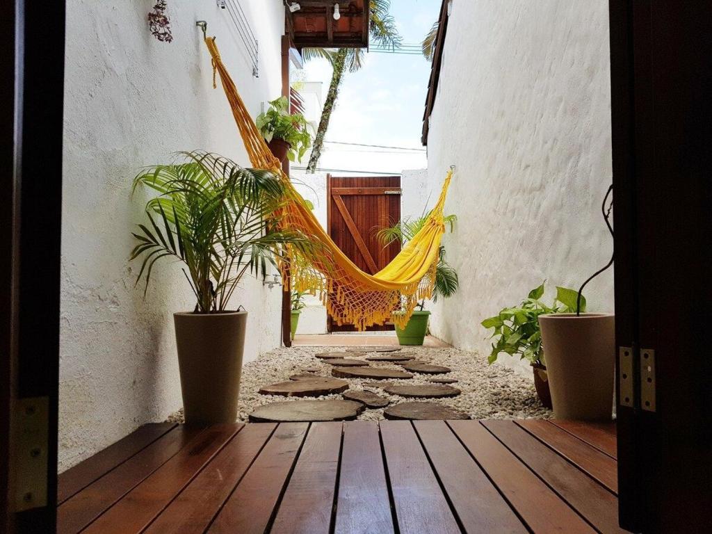 Entrada do Suíte D&K Queen. Um deck, vasos com plantas, uma estrada de pedra com uma rede e no fundo a porta de madeira.