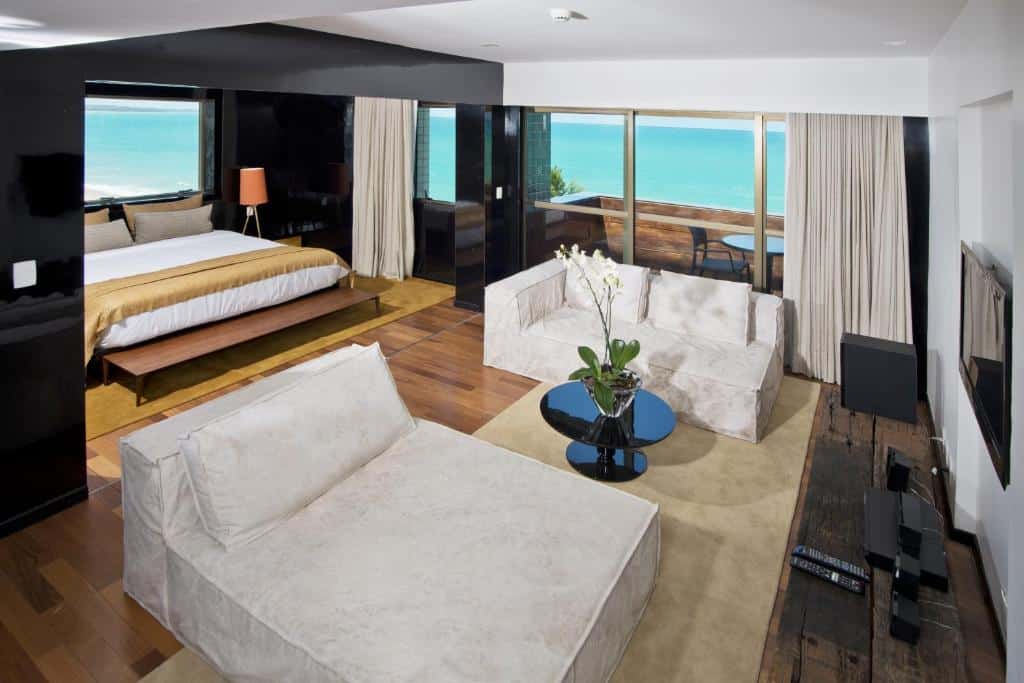 Suíte presidencial do Ritz Lagoa da Anta, de 120 m². Há uma área com a cama de casal grande e uma sala de estar com sofás espaçosos brancos. Há também uma sacada com mesa de duas cadeiras e vista de frente para o mar