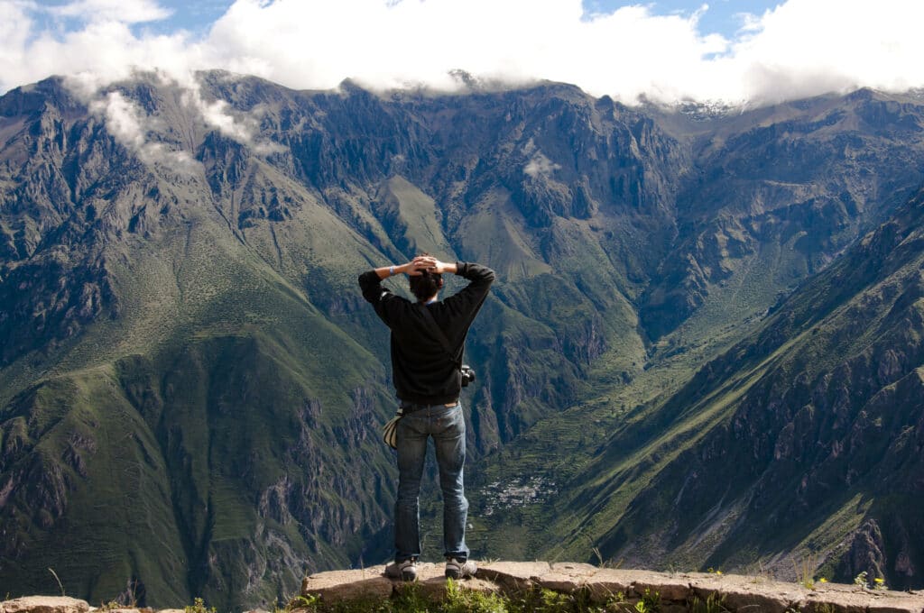 Homem com as duas mãos na cabeça, de costas, olhando os cânions do colca, em Arequipa, Peru