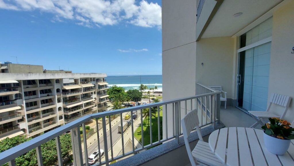 Varanda do Hospedagem de luxo no Barra Palace – Rio Paraíso durante o dia com mesa redonda do lado direito da cama com duas cadeiras com vista para a rua e praia.