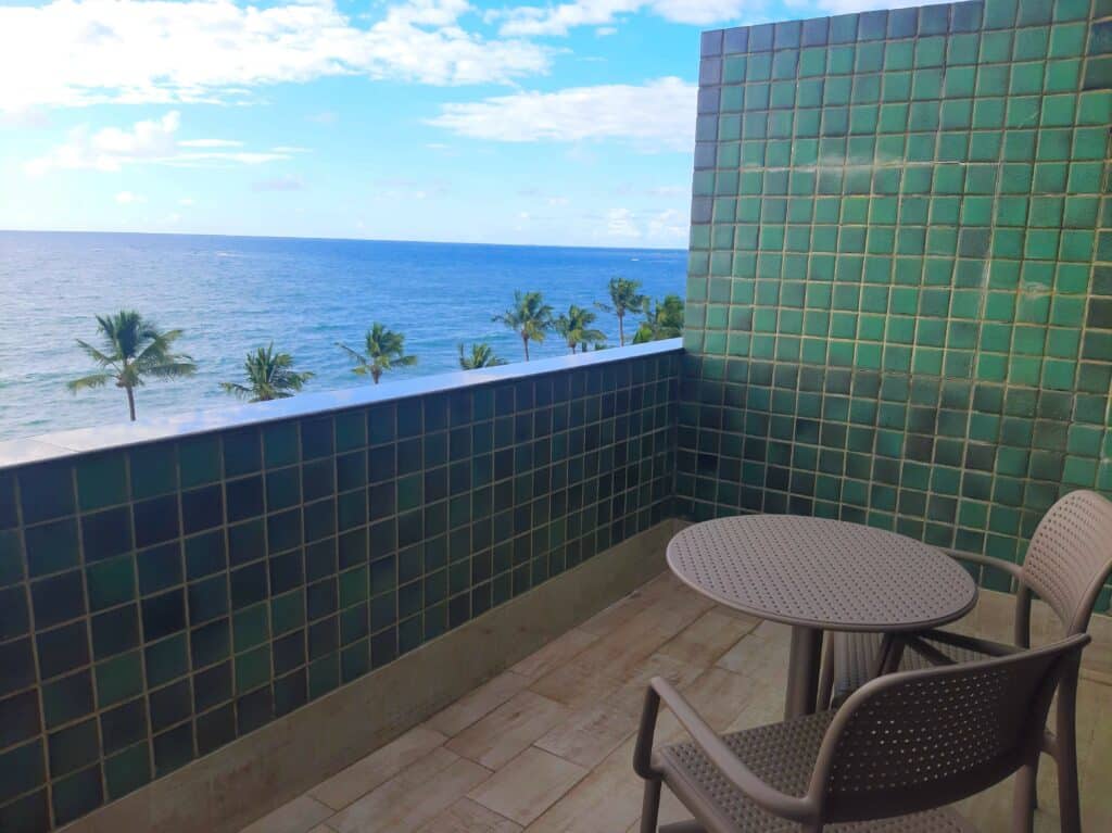 varanda com vista de frente para o mar do quarto Design floor do Ritz Lagoa da Anta. O ambiente tem uma mesa redonda com duas cadeiras e vista do mar com coqueiros na orla