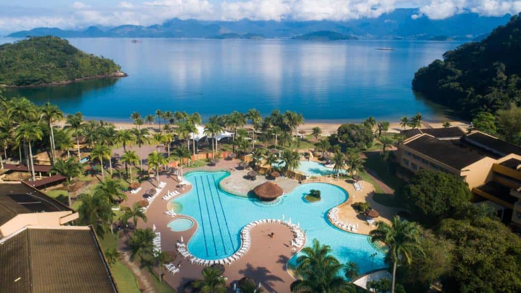 Vila Galé Eco Resort Angra visto de cima. No centro estão as piscinas rodeadas de coqueiros e ao fundo está o mar. Imagem para ilustrar o post airbnb em Angra dos Reis.