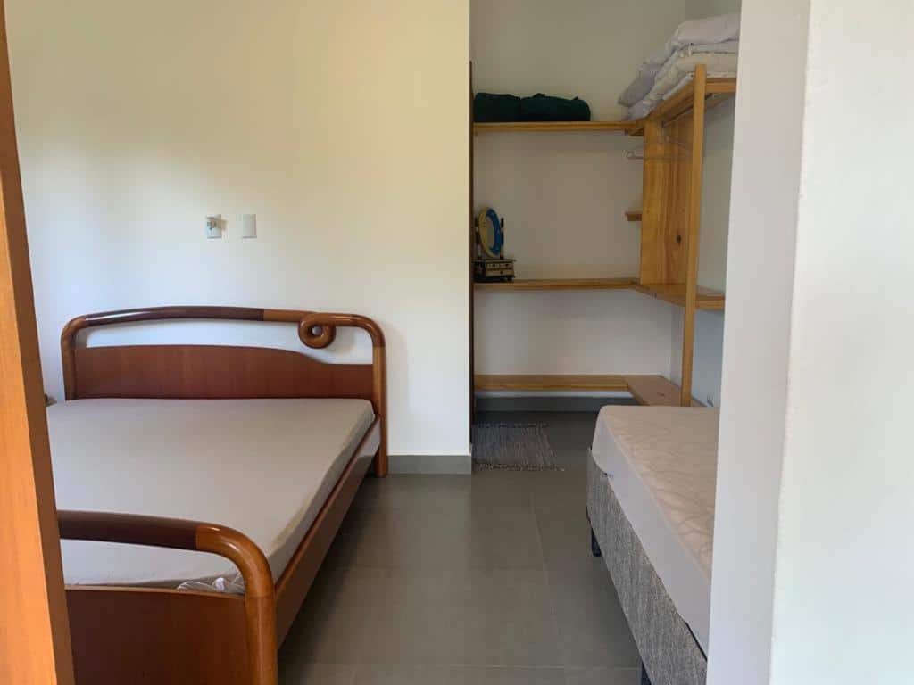 Quarto da Vila Itamambuca Apto Passarinhos. Uma cama de solteiro do lado direito, no fundo prateleiras, do lado esquerdo uma cama de casal.