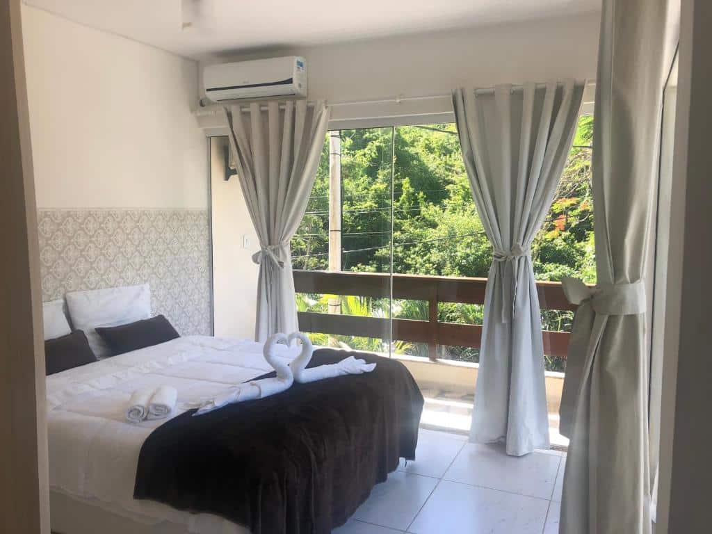 Quarto da casa Villa Bella Vista. A cama de casal está no lado esquerdo e o quarto é rodeado de paredes de vidro que dão acesso a varanda. Imagem para ilustrar o post airbnb em Cabo Frio.