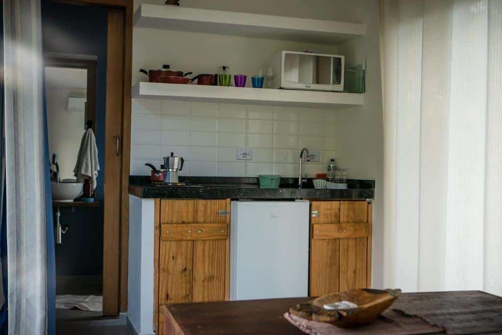 Villa Dallê - Terreo - Vila Itamambuca. Uma mesa de centro na frente, atrás a pia com um frigobar, micro-ondas e utensílios de cozinha do lado direito. Do lado esquerdo a porta do banheiro.