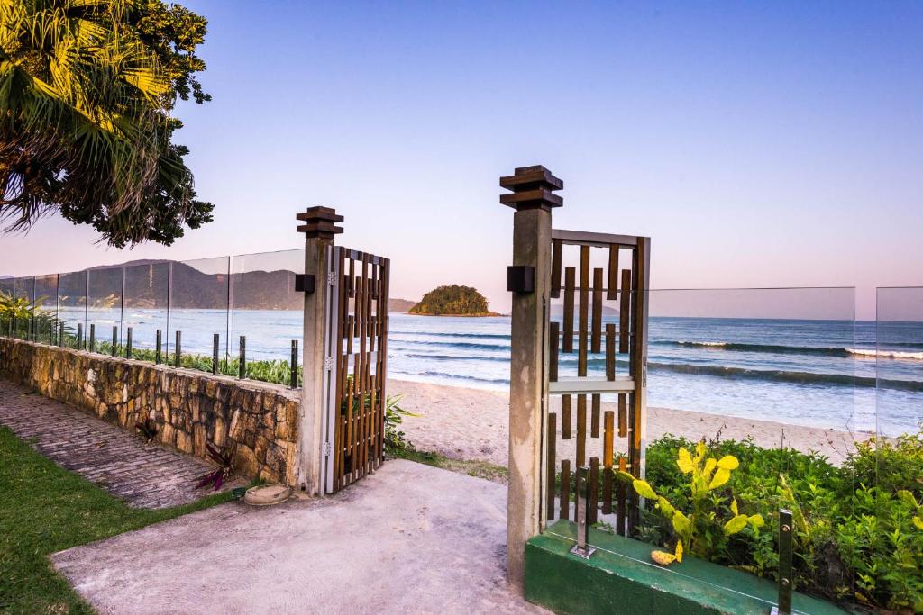 Vista do mar por muro de vidro, com portão aberto ao centro, de onde se tem acesso direto exclusivo da Villa Sapê Pousada à Praia do Sapê
