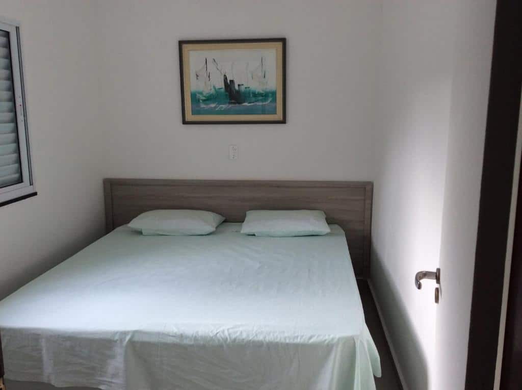 Quarto do VILLAGE 4 CASAS PÉ NA AREIA 8 PAX, um dos airbnb em Barequeçaba. A cama de casal está no centro do quarto e possui um quadrinho na parede acima. Ao lado esquerdo fica uma janela.