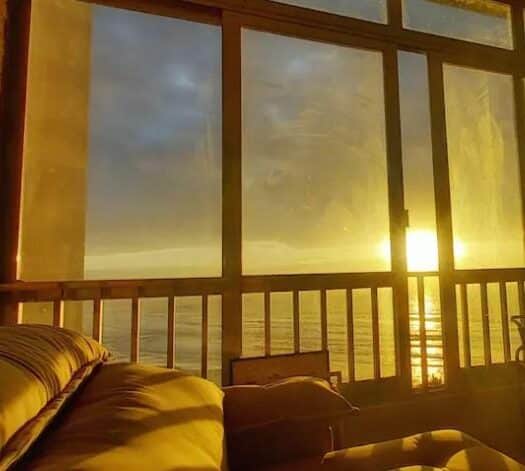 Uma janela grande e extensa com vista para o mar no Guarujá, de dentro de um apartamento. O sol se põe.