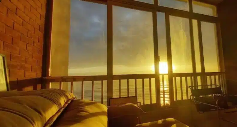 Uma janela grande e extensa com vista para o mar no Guarujá, de dentro de um apartamento. O sol se põe.
