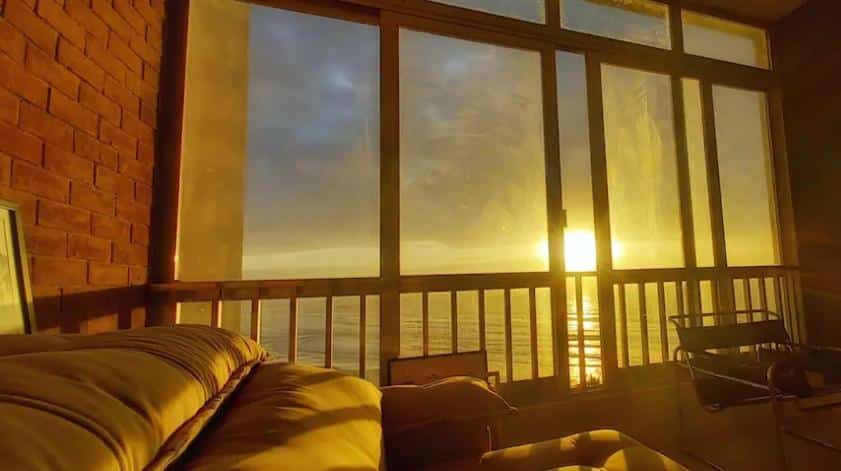 Uma janela grande e extensa com vista para o mar no Guarujá, de dentro de um apartamento. O sol se põe.