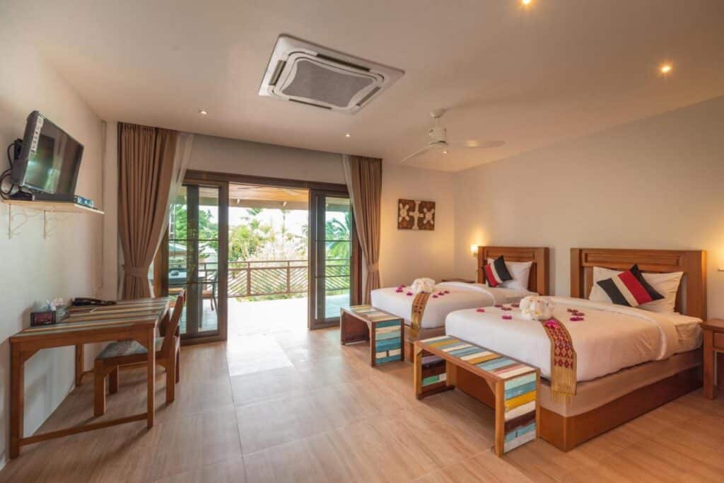 Quarto do Wandee Garden com duas camas de solteiro, uma escrivaninha, uma TV montada na parede e portas de vidro deslizantes que levam a uma varanda com vista para o jardim.