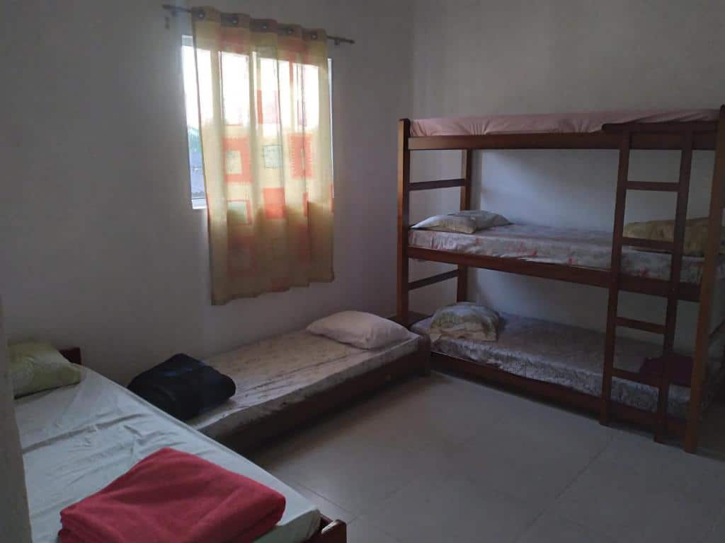 Quarto do Xixová Hostel. Uma treliche do lado direito, no meio uma cama de solteiro, do lado esquerdo outra cama de solteiro. No meio, em cima, uma janela. Foto para ilustrar post sobre pousadas em São Vicente.