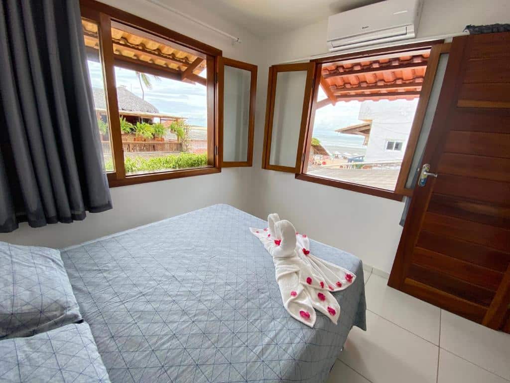 Foto do quarto do Acoara PRAIA. Representa o post sobre airbnb em Jericoacoara. Vemos o ambiente de cima. A cama é de casal e está no canto esquerdo. À sua frente há duas grandes janelas com vista para o mar. Há uma porta na direita.
