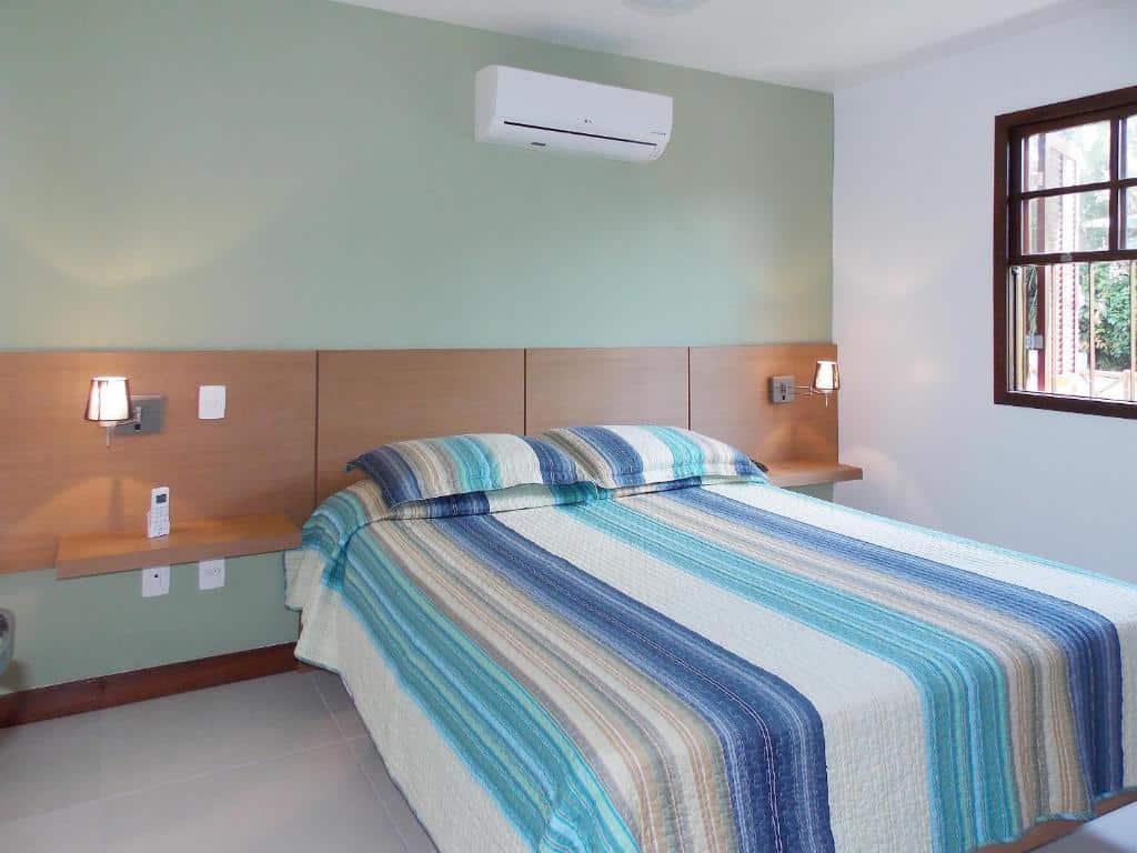 Quarto do airbnb Ancoradouro Flats. A cama está centralizada no quarto e no lado direito há uma janela. Imagem para ilustrar o post airbnb em Ilha Grande.