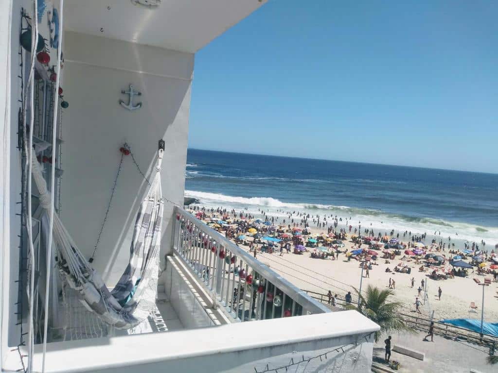 Uma sacada do Apartamento temporada, em Maricá, do lado esquerdo com rede, do lado direito a praia com muitas pessoas.