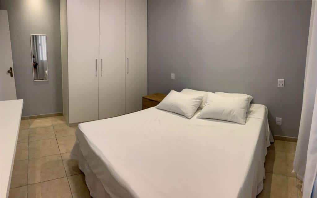 Foto do quarto do Apartamento ao lado da UFOP com garagem. Ilustra o post sobre airbnb em Ouro Preto. A cama de casal está no centro. Do lado esquerdo há um guarda-roupa, espelho e porta, e na direita vemos um relance da cortina.