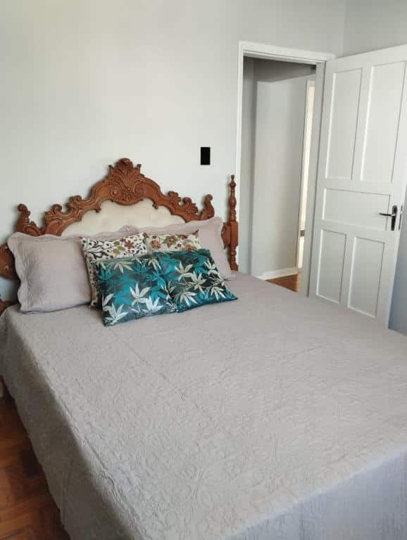 Foto do quarto em Apartamento encantador no centro c/ garagem. Há uma cama de casal com cabeceira ornamentada em estilo clássico, e uma porta branca está à sua direita.
Ilustra o post sobre airbnb em Serra Negra.