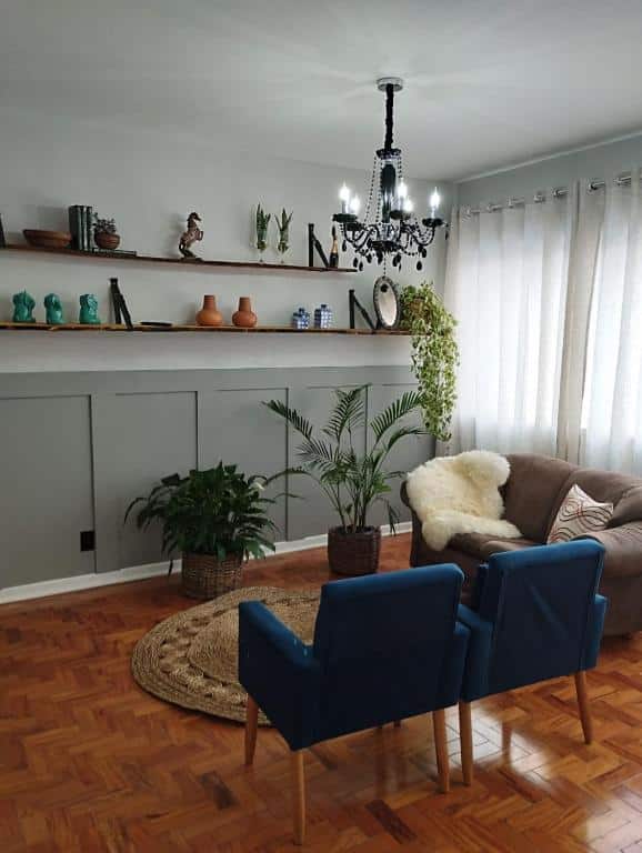 Foto da sala de estar em Apartamento encantador no centro c/ garagem. Há um sofá com manta na direita, atrás dele há uma janela. Do lado do sofá há duas poltronas azuis, no centro da sala. De frente para eles há uma parede com estantes e várias decorações.